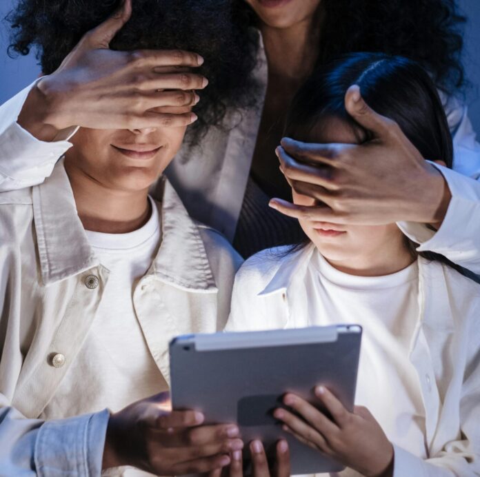 Mother covering eyes of her children with hands against internet content on digital pad